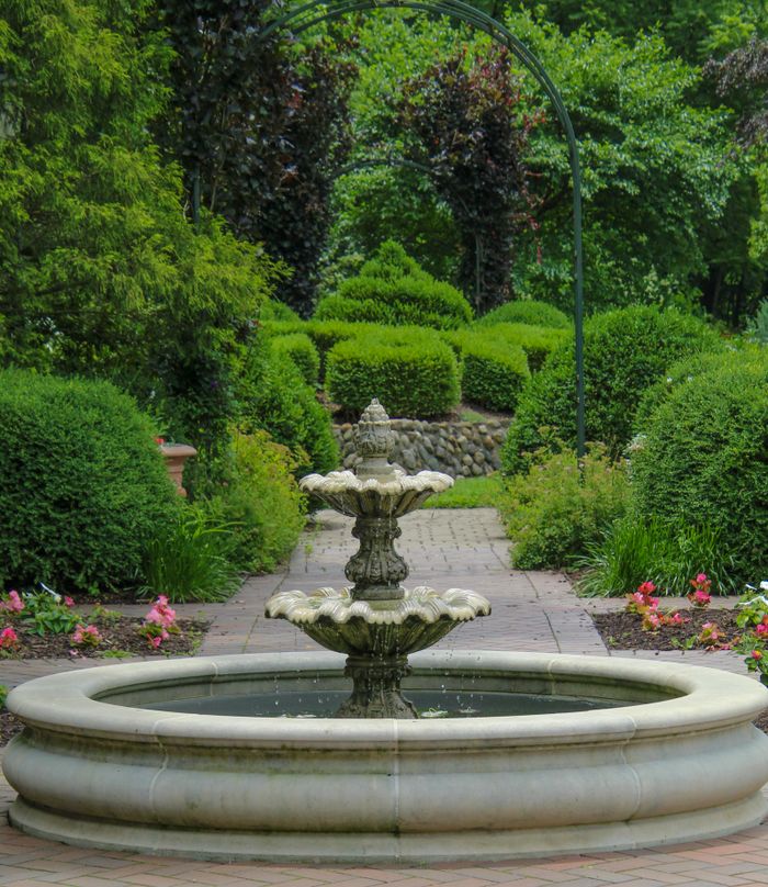 Beautiful stone fountain in a tranquil garden with lush green shrubs and colorful flowers in summer.
